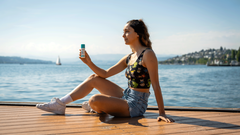 Girl sitting next to the lake holding a suncream