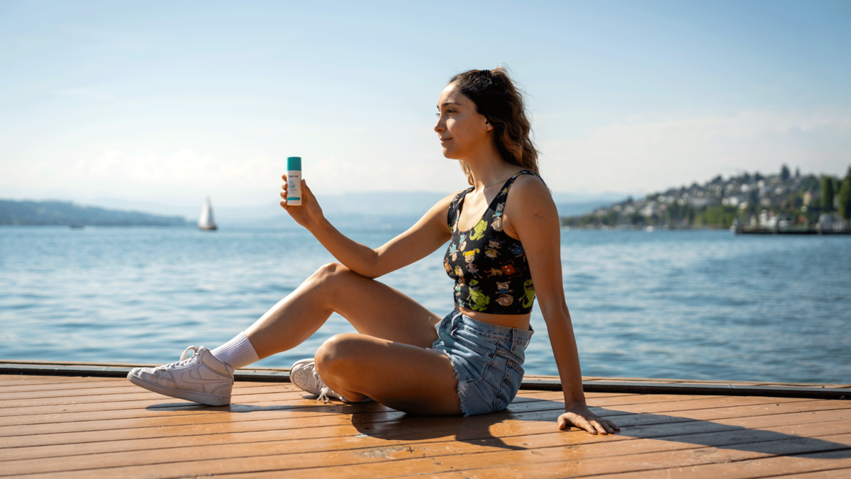 Girl sitting next to the lake, holding a suncream